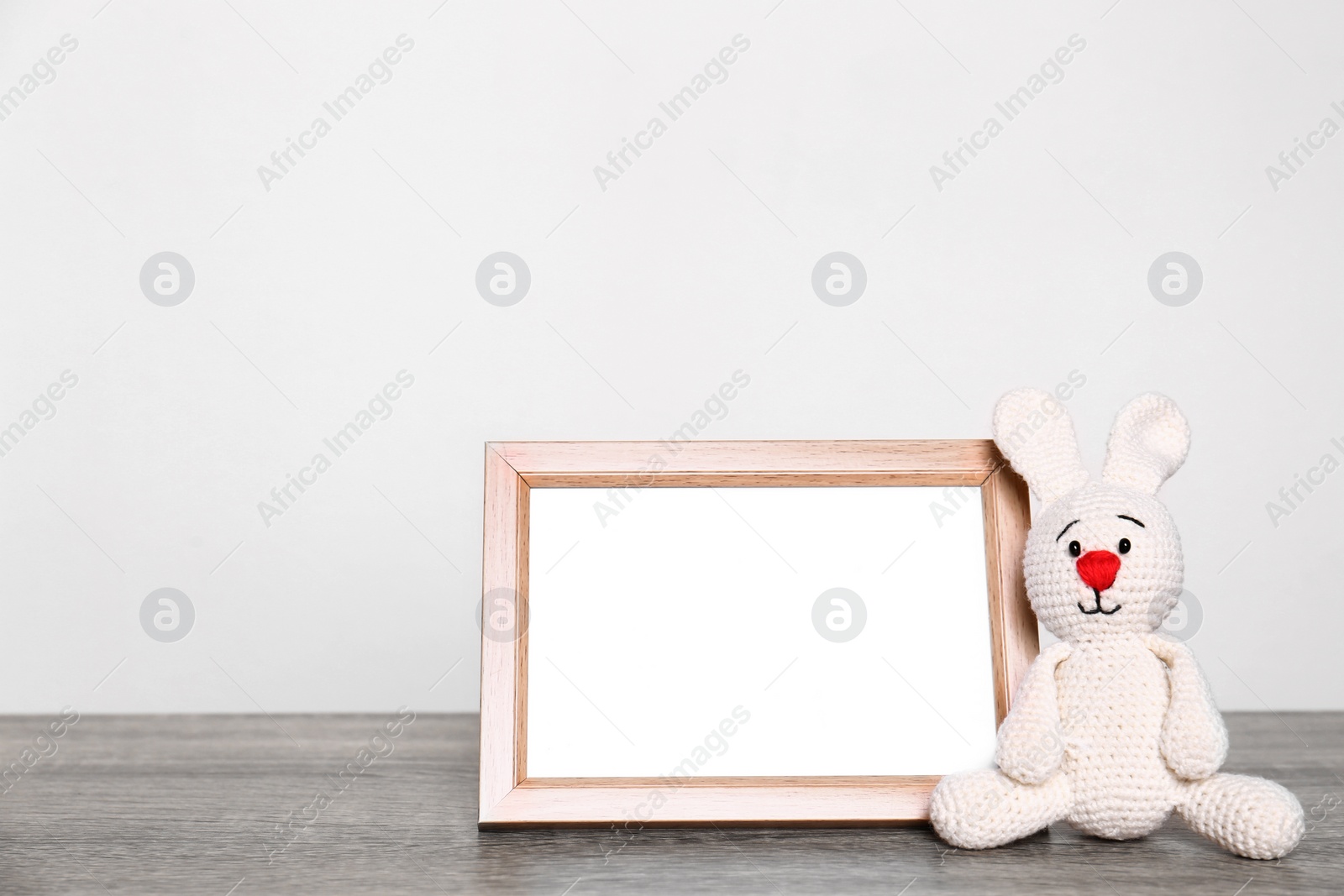 Photo of Photo frame and adorable toy bunny on table against light background, space for text. Child room elements