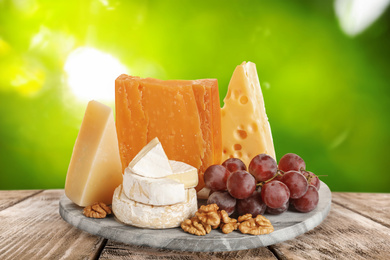 Different types of delicious cheeses on wooden table outdoors. Dairy products