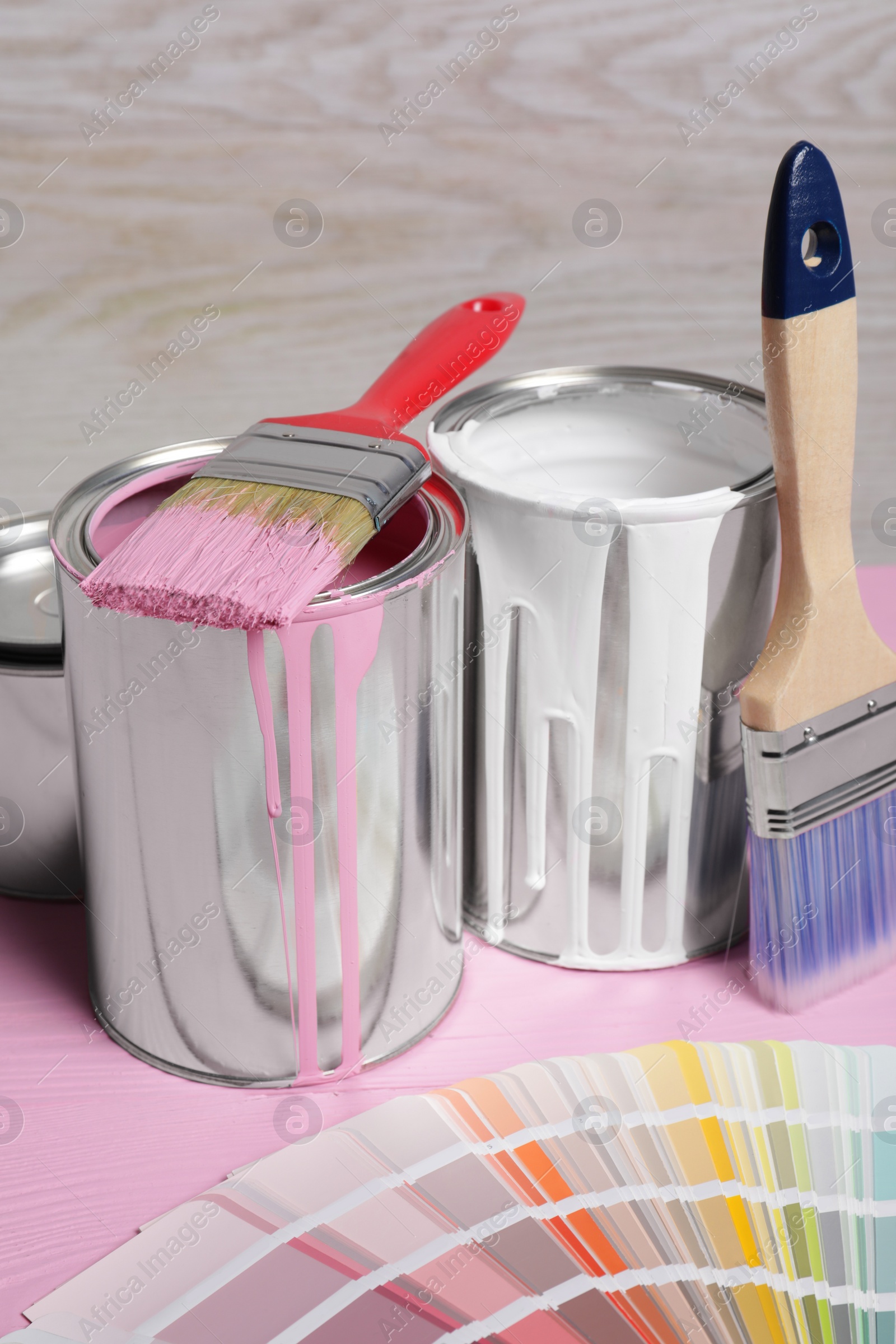 Photo of Cans of paints, brushes and color palette on pink wooden table