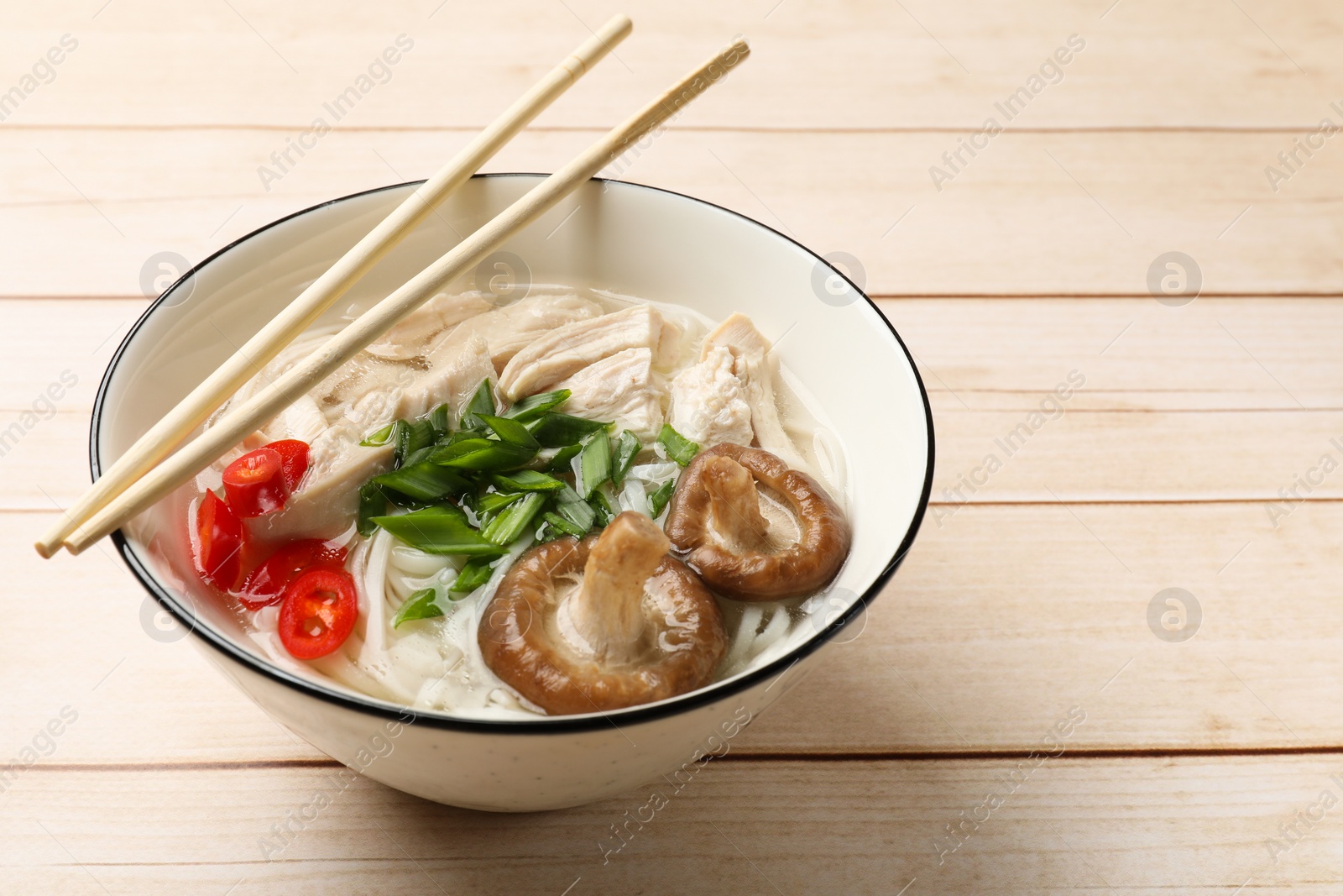 Photo of Delicious ramen with meat in bowl and chopsticks on wooden table. Space for text