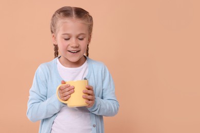 Happy girl with yellow ceramic mug on beige background, space for text