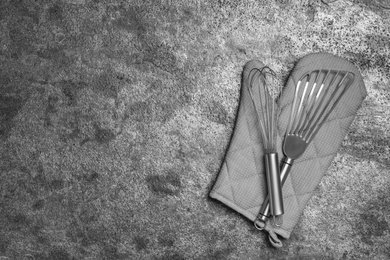 Photo of Slotted turner, whisk and oven mitt on grey table, top view with space for text. Cooking utensils