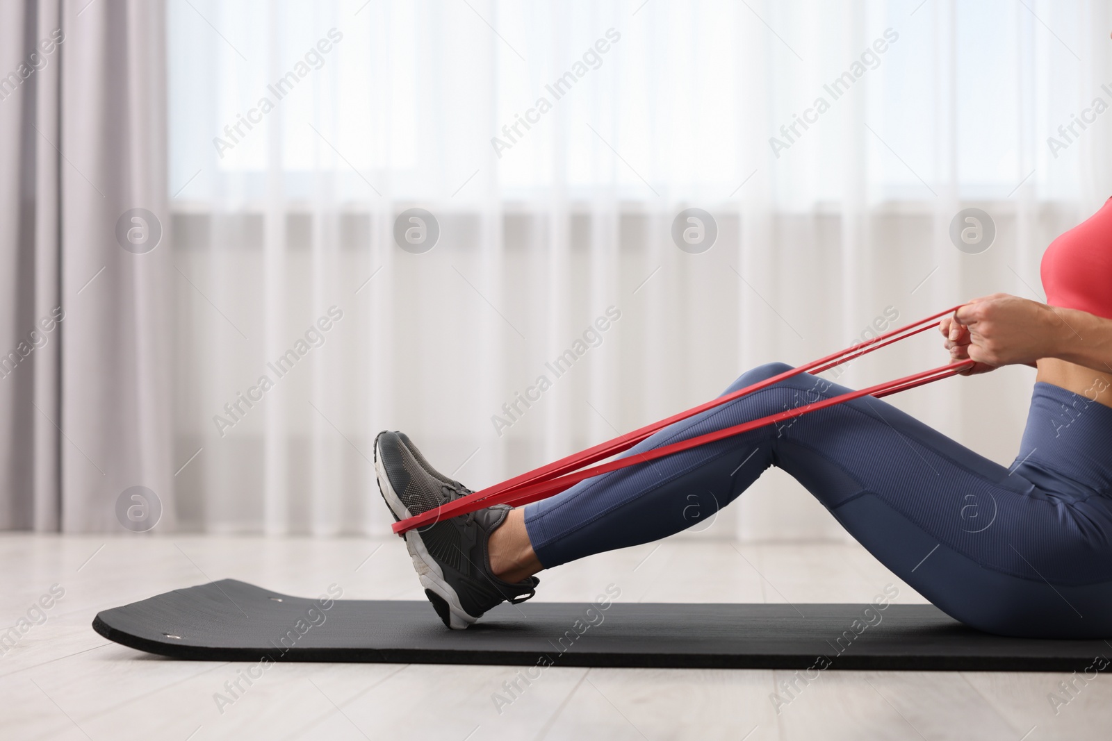 Photo of Woman doing exercise with fitness elastic band on mat indoors, closeup
