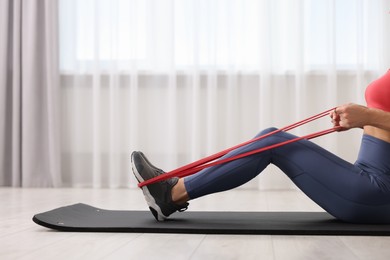 Woman doing exercise with fitness elastic band on mat indoors, closeup