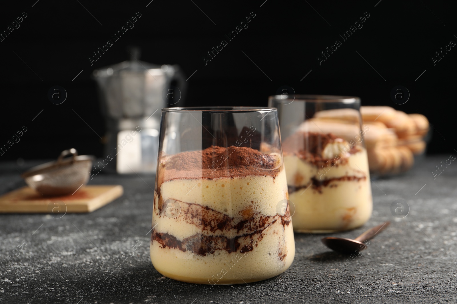 Photo of Delicious tiramisu in glasses on grey textured table, closeup