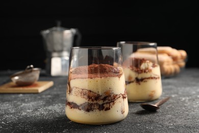 Photo of Delicious tiramisu in glasses on grey textured table, closeup