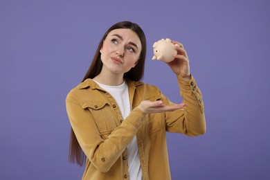 Photo of Sad woman with piggy bank on purple background