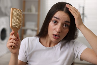 Emotional woman with brush examining her hair in bathroom. Dandruff problem