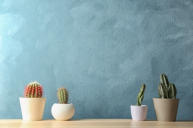 Different potted cacti on table near color background, space for text. Interior decor