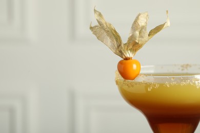 Photo of Refreshing cocktail decorated with physalis fruit on light background, closeup. Space for text
