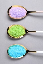Spoons with colorful sea salt on light grey table, flat lay