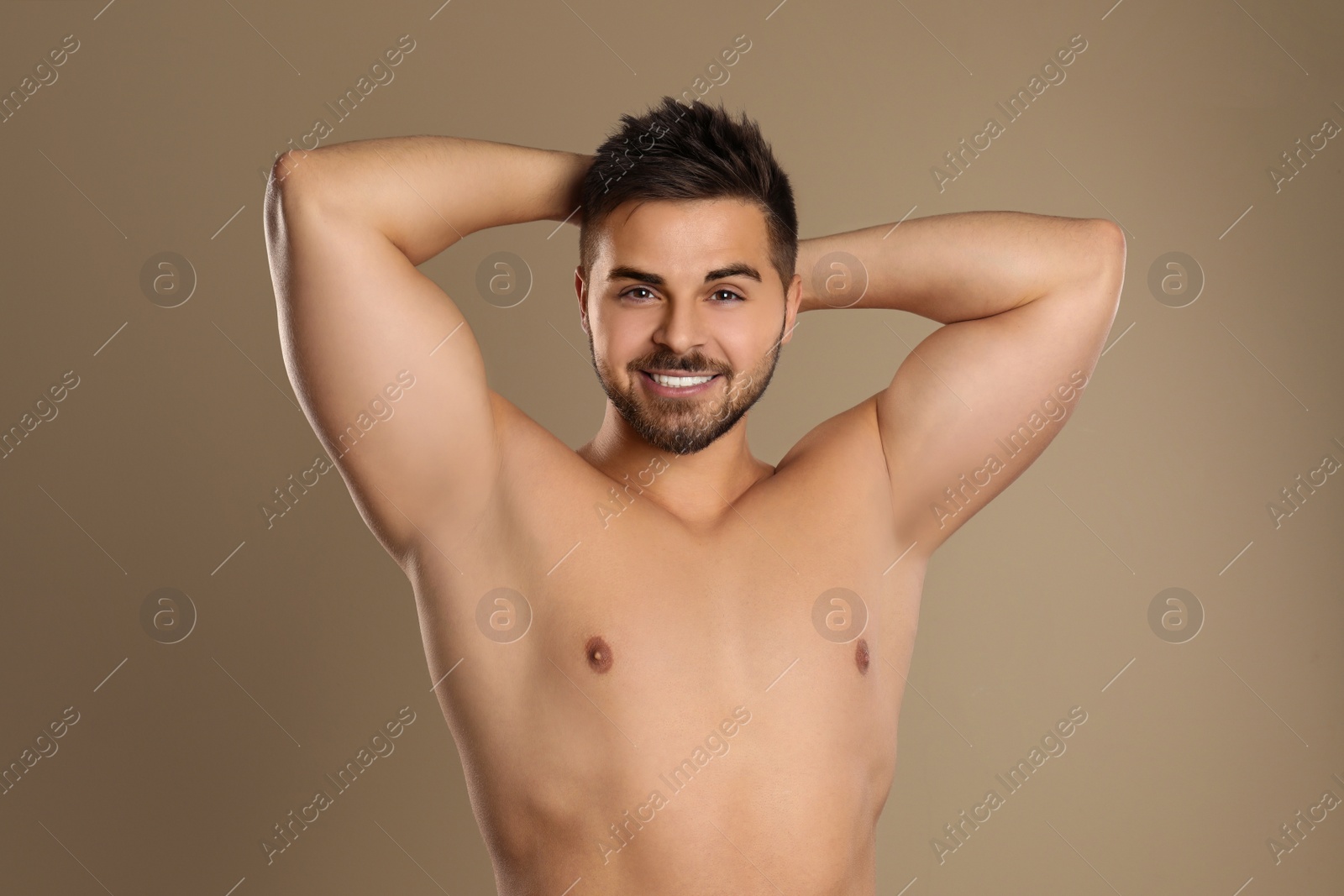 Photo of Young man showing hairless armpits after epilation procedure on brown background