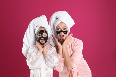 Photo of Emotional mother and daughter with black facial masks on pink background