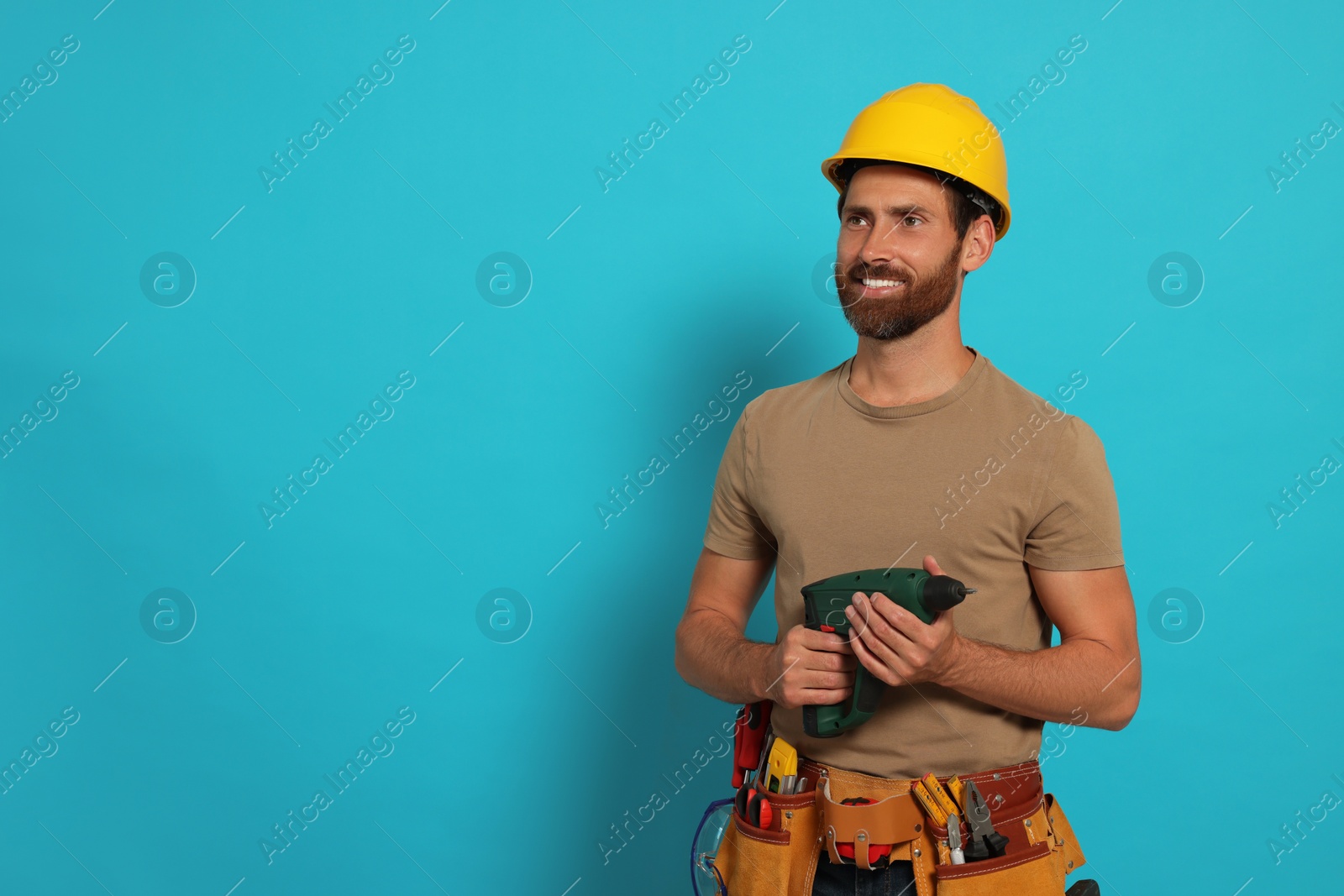 Photo of Professional builder in hard hat with tool belt and power drill on light blue background, space for text