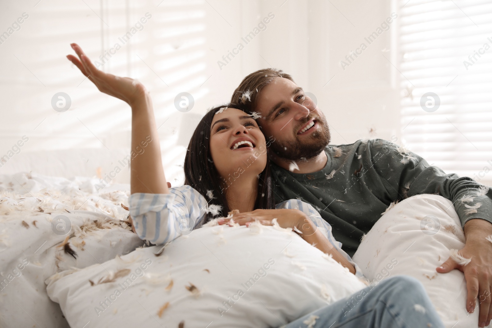 Photo of Happy young couple resting after fun pillow fight in bedroom