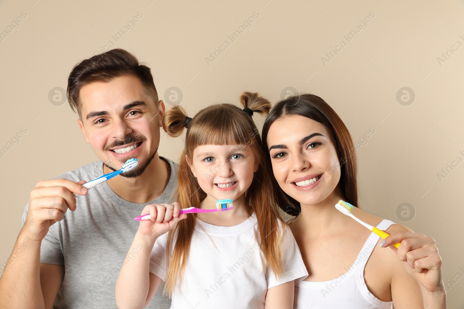 Photo of Little girl and her parents brushing teeth together on color background