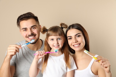 Little girl and her parents brushing teeth together on color background