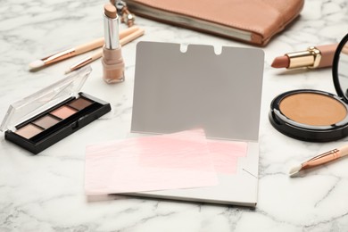 Photo of Facial oil blotting tissues and different decorative cosmetics on white marble table. Mattifying wipes