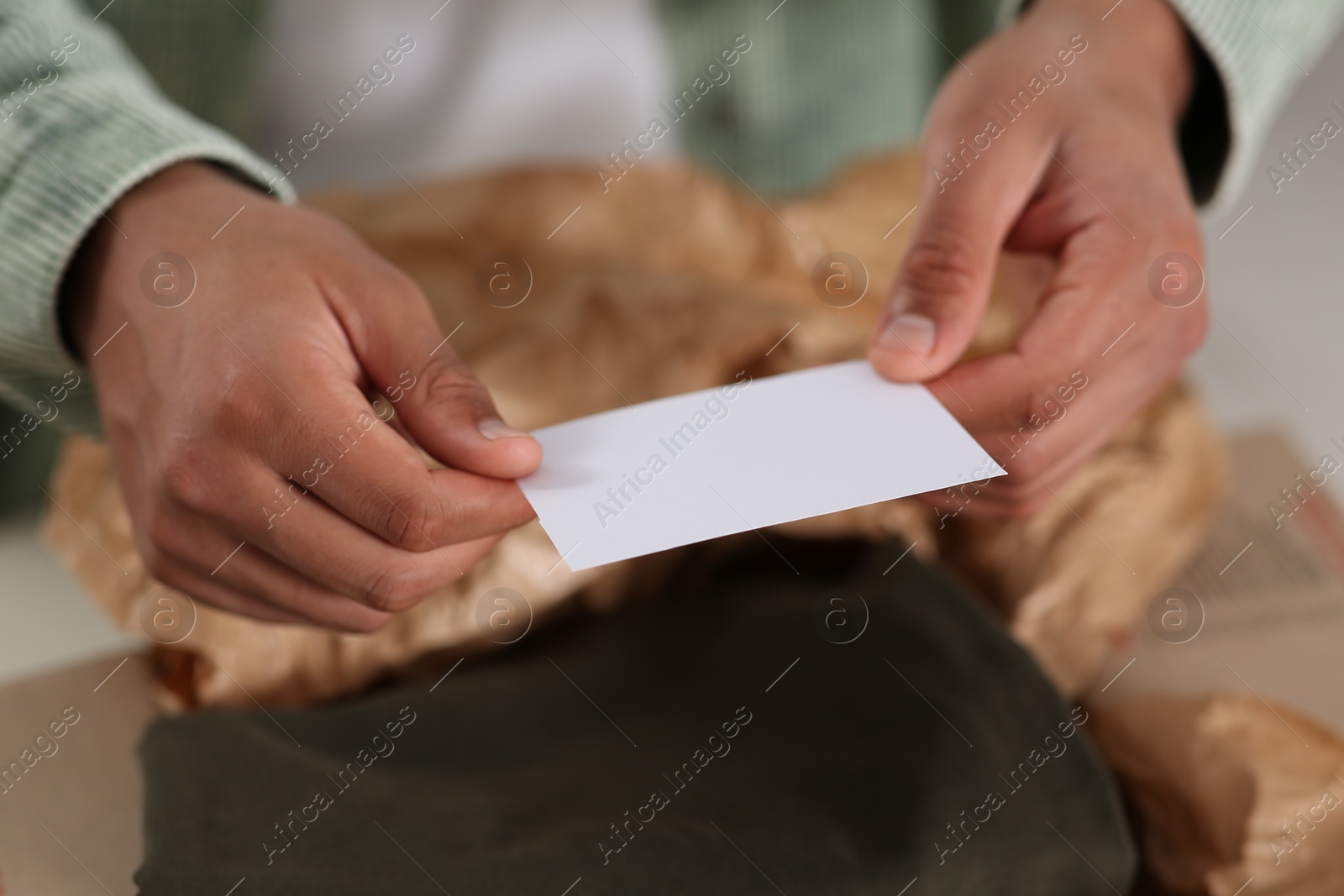 Photo of Young man holding greeting card near parcel with Christmas gift, closeup