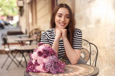 Beautiful woman with bouquet of spring flowers in outdoor cafe