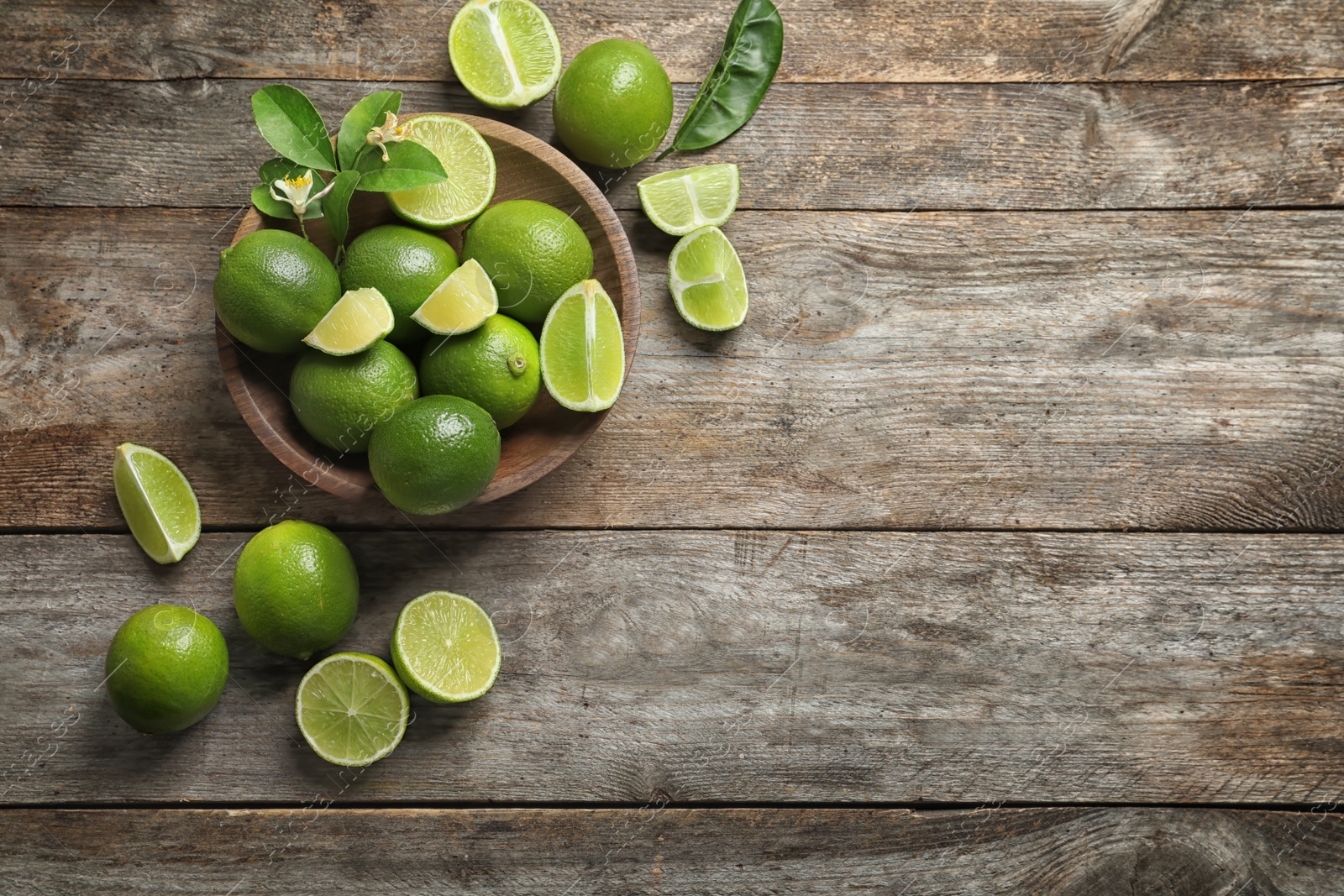 Photo of Bowl with fresh ripe limes on wooden background, top view