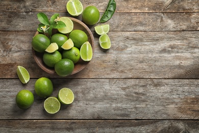 Photo of Bowl with fresh ripe limes on wooden background, top view