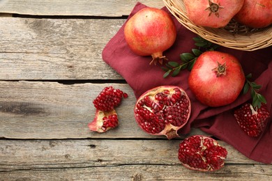 Photo of Fresh pomegranates and green leaves on wooden table, top view. Space for text