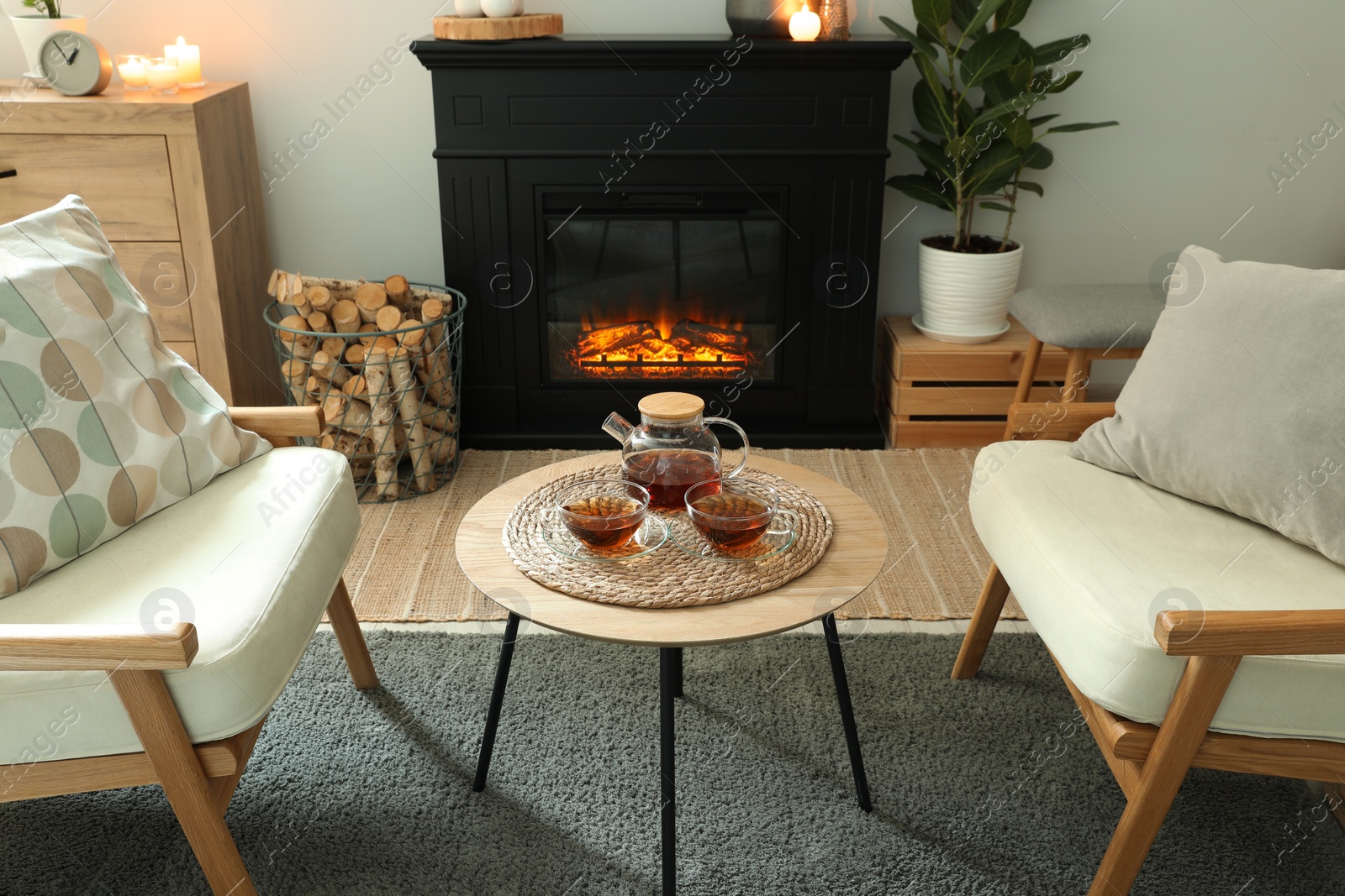 Photo of Stylish fireplace near comfortable armchairs and coffee table with tea in cosy living room. Interior design