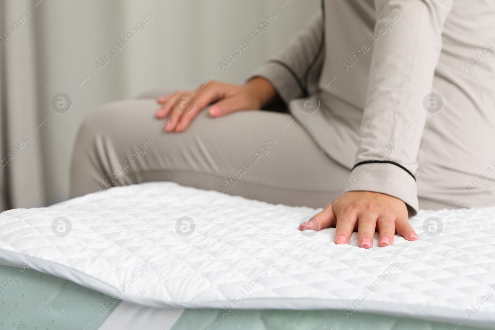 Photo of Woman sitting on new soft mattress indoors, closeup