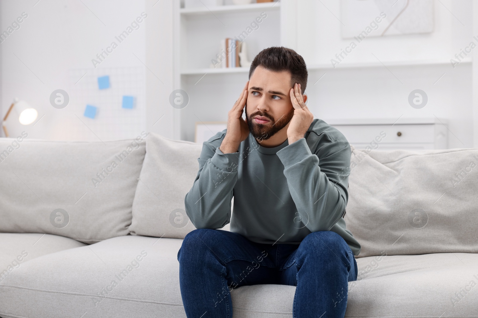 Photo of Man suffering from headache on sofa at home