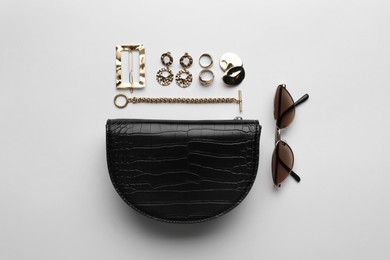 Photo of Stylish woman's bag, sunglasses and bijouterie on light background, flat lay