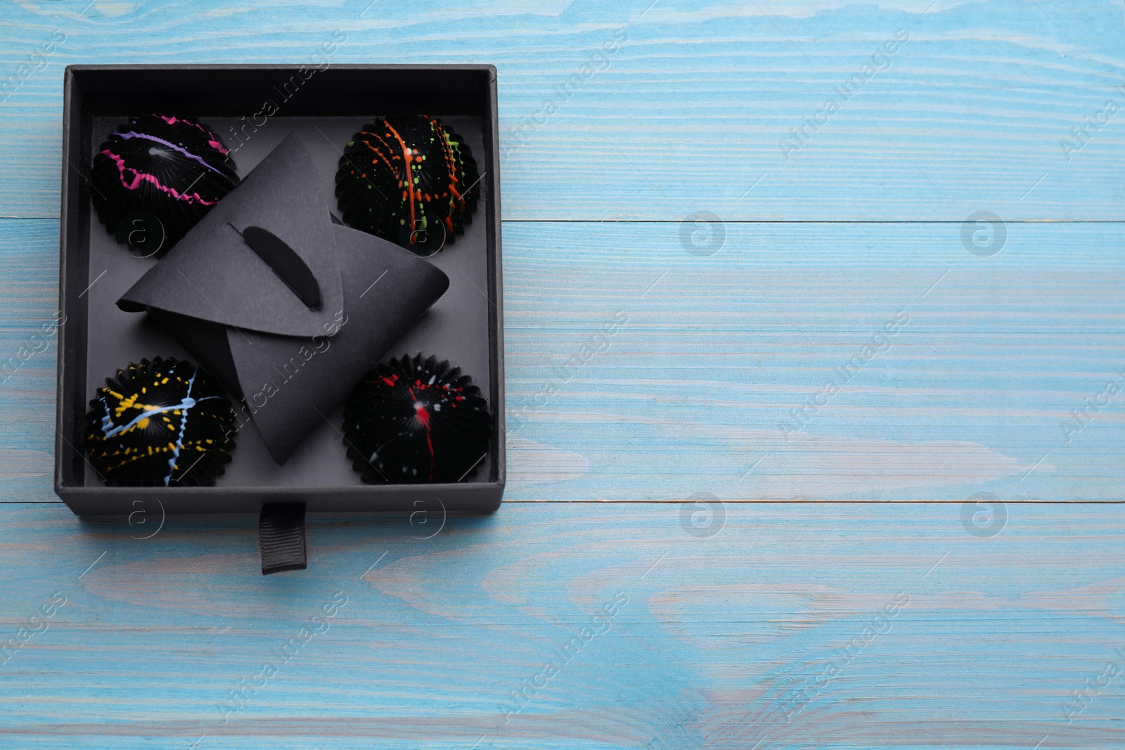 Photo of Box of tasty chocolate candies on light blue wooden table, top view. Space for text