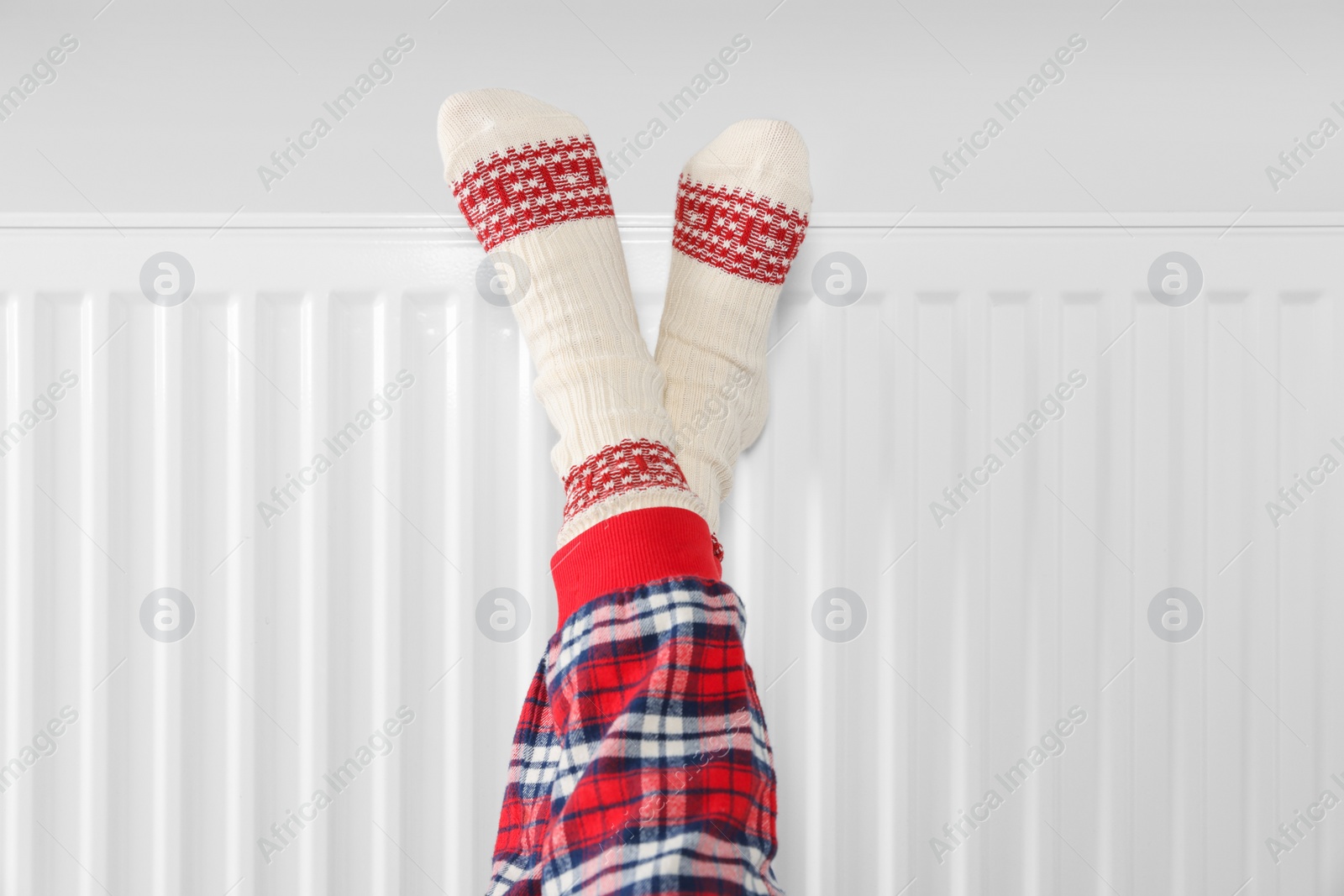 Photo of Little girl warming feet near heating radiator indoors, closeup