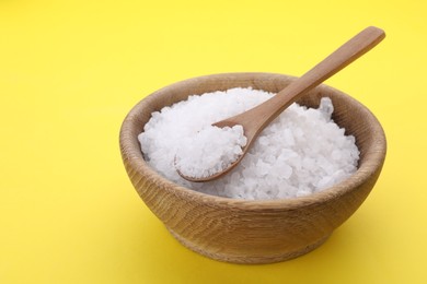 Photo of Bowl and spoon with sea salt on yellow background, closeup