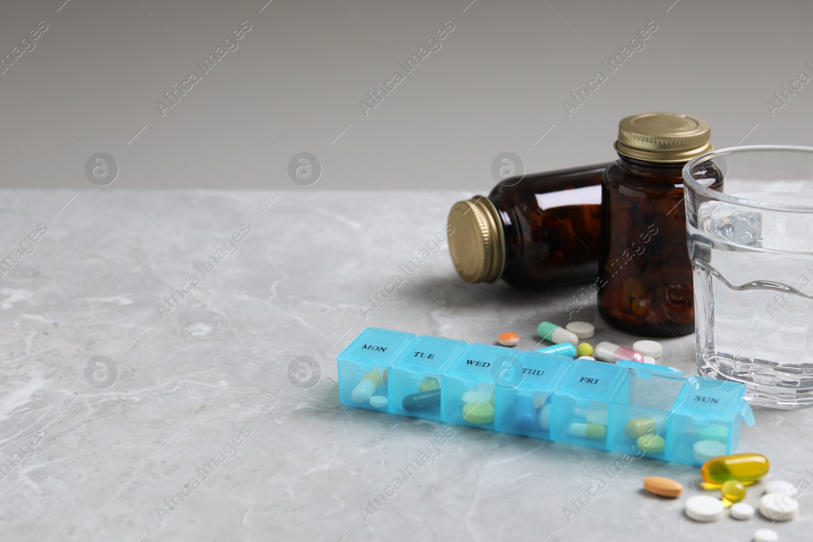 Photo of Weekly pill box with medicaments and glass of water on grey marble table. Space for text