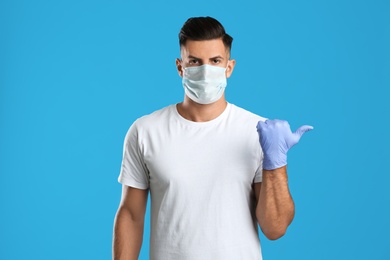 Man in protective face mask and medical gloves pointing at something on blue background
