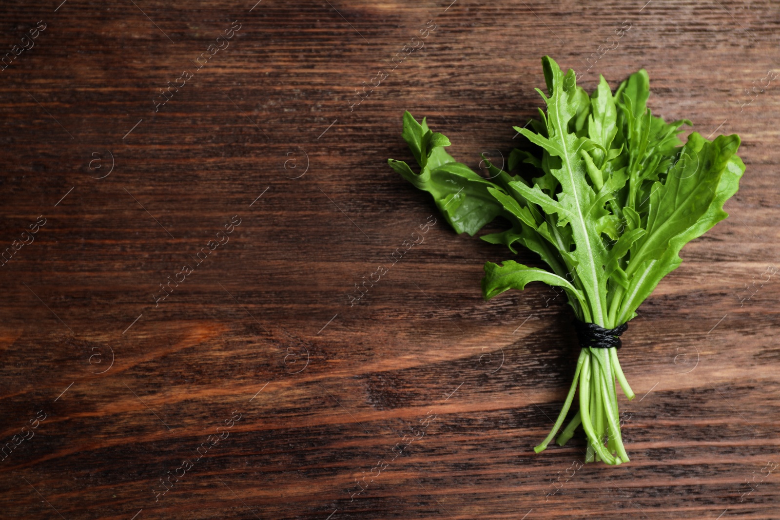 Photo of Fresh arugula on wooden table, top view. Space for text