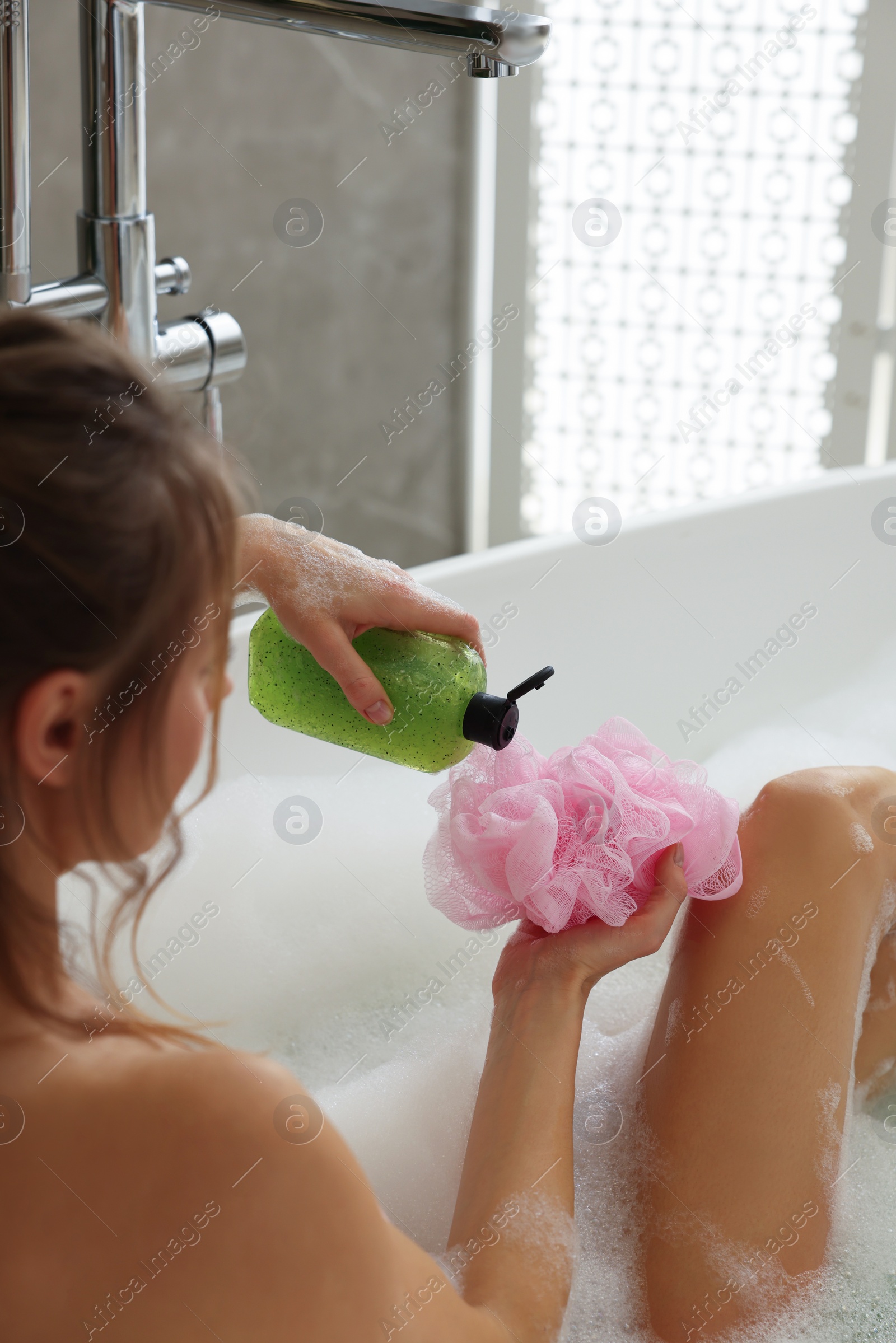 Photo of Woman pouring shower gel onto mesh pouf in bath indoors