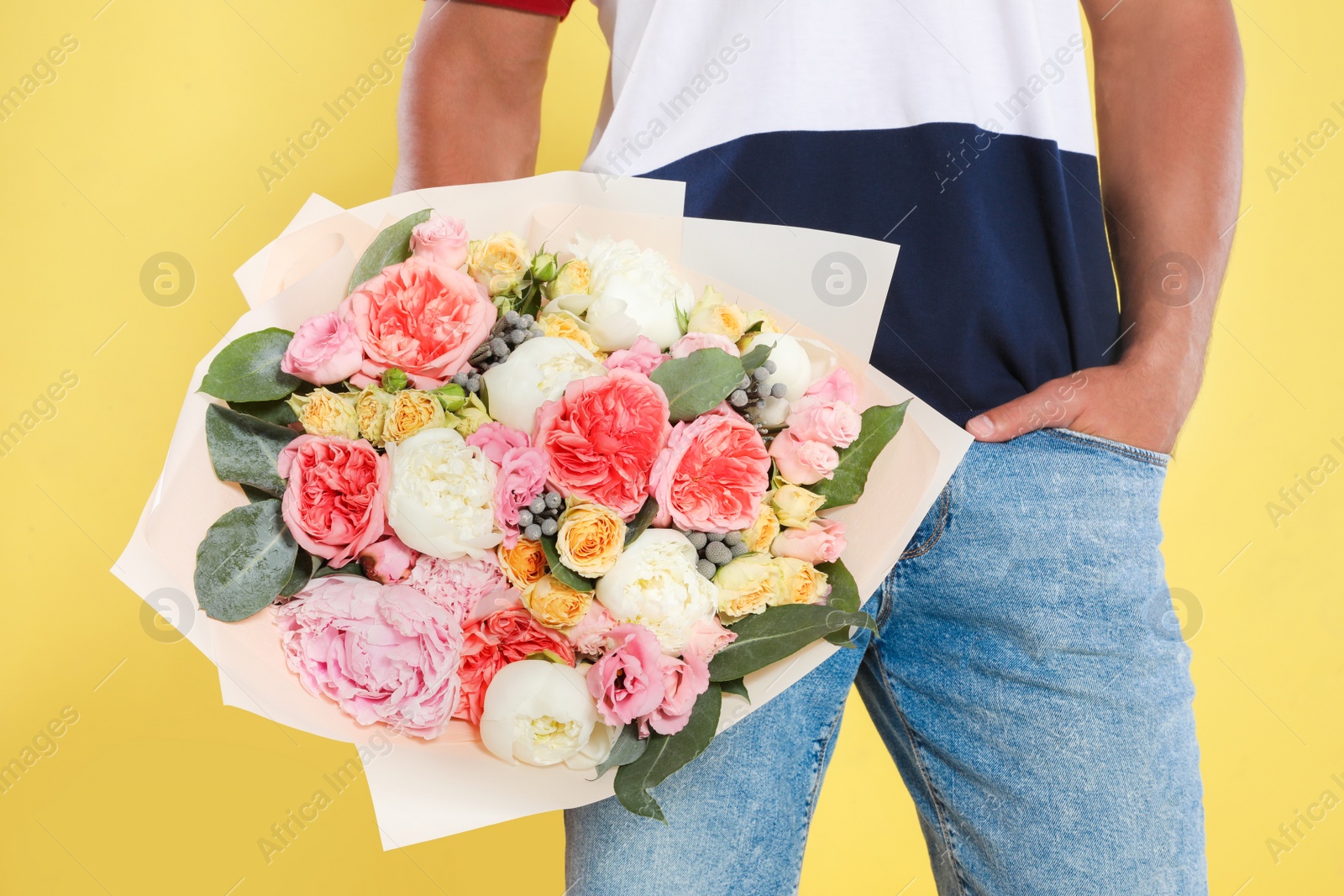 Photo of Young handsome man with beautiful flower bouquet on yellow background, closeup view