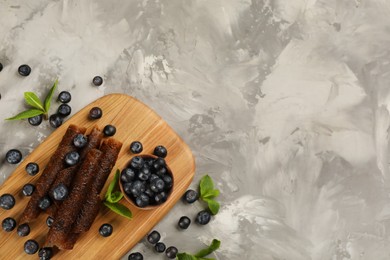 Photo of Delicious fruit leather rolls and blueberries on grey table, flat lay. Space for text
