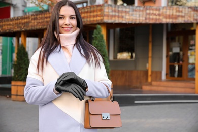 Photo of Portrait of beautiful young woman with leather gloves and stylish bag on city street