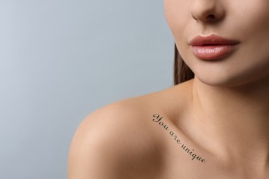 Image of Affirmation. Woman with tattooed phrase You Are Unique on collarbone against light grey background, closeup. Space for text