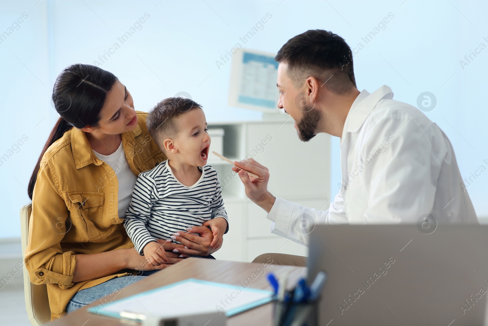 Photo of Mother and son visiting pediatrician in hospital. Doctor examining little boy