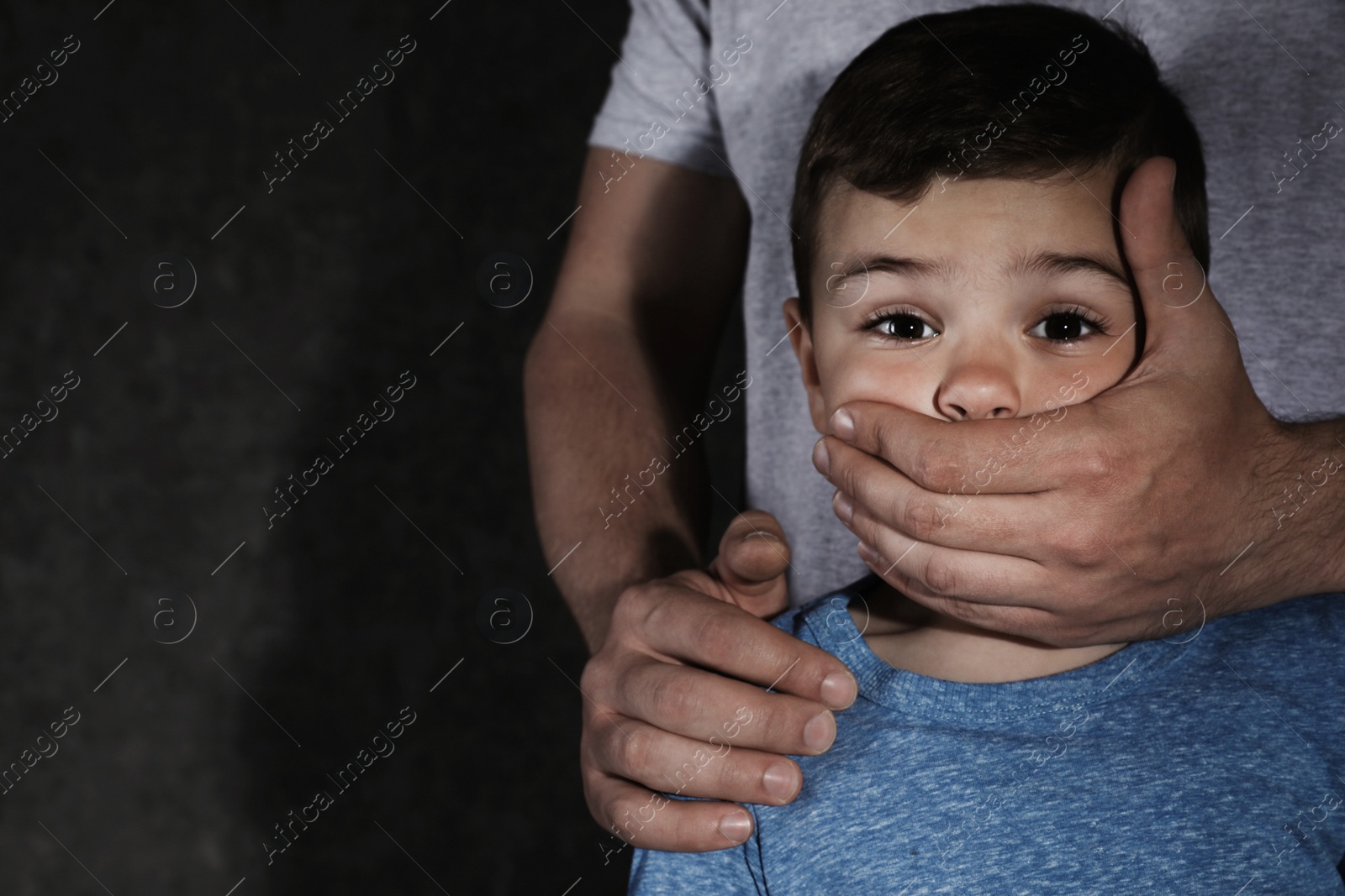 Photo of Adult man covering scared little boy's mouth on dark background, space for text. Child in danger