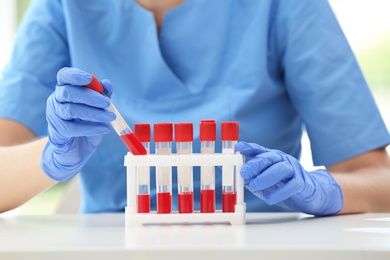 Photo of Scientist holding test tube with blood sample at table in laboratory