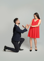 Young woman rejecting engagement ring from boyfriend on light grey background