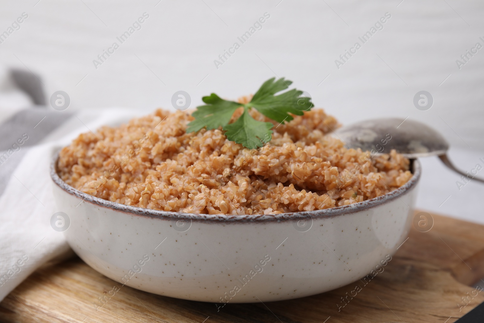 Photo of Tasty wheat porridge with parsley in bowl on wooden table, closeup