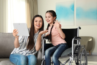 Photo of Girl in wheelchair and her mother using video chat on tablet at home