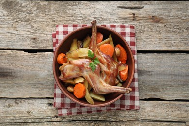 Photo of Tasty cooked rabbit with vegetables in bowl on wooden table, top view