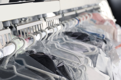 Photo of Hangers with clothes on garment conveyor at dry-cleaner's, closeup